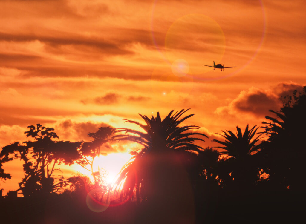 Malibu sunset my the Malibu Pier. Small plane flying over the sun. Bright orange sunset.